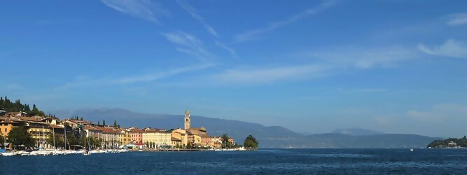 Get my Trip Tirol beliebte Urlaubsziele am Gardasee -  Mit einer Fläche von 370 km² ist der Gardasee der größte See Italiens. Es liegt am Fuße der Alpen und erstreckt sich über drei Staaten: Lombardei, Venetien und Trentino. Die maximale Tiefe des Sees beträgt 346 m, er hat eine längliche Form und sein nördliches Ende ist sehr schmal. Dort ist der See von den Bergen der Gruppo di Baldo umgeben. Du trittst aus deinem gemütlichen Hotelzimmer und es begrüßt dich die warme italienische Sonne. Du blickst auf den atemberaubenden Gardasee, der in zahlreichen Blautönen schimmert - von tiefem Dunkelblau bis zu funkelndem Türkis. Majestätische Berge umgeben dich, während die Brise sanft deine Haut streichelt und der Duft von blühenden Zitronenbäumen deine Nase kitzelt. Du schlenderst die malerischen, engen Gassen entlang, vorbei an farbenfrohen, blumengeschmückten Häusern. Vereinzelt unterbricht das fröhliche Lachen der Einheimischen die friedvolle Stille. Du fühlst dich wie in einem Traum, der nicht enden will. Jeder Schritt führt dich zu neuen Entdeckungen und Abenteuern. Du probierst die köstliche italienische Küche mit ihren frischen Zutaten und verführerischen Aromen. Die Sonne geht langsam unter und taucht den Himmel in ein leuchtendes Orange-rot - ein spektakulärer Anblick.